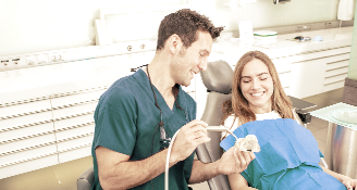 Dentist explaining dental procedure to smiling female patient using a model of teeth