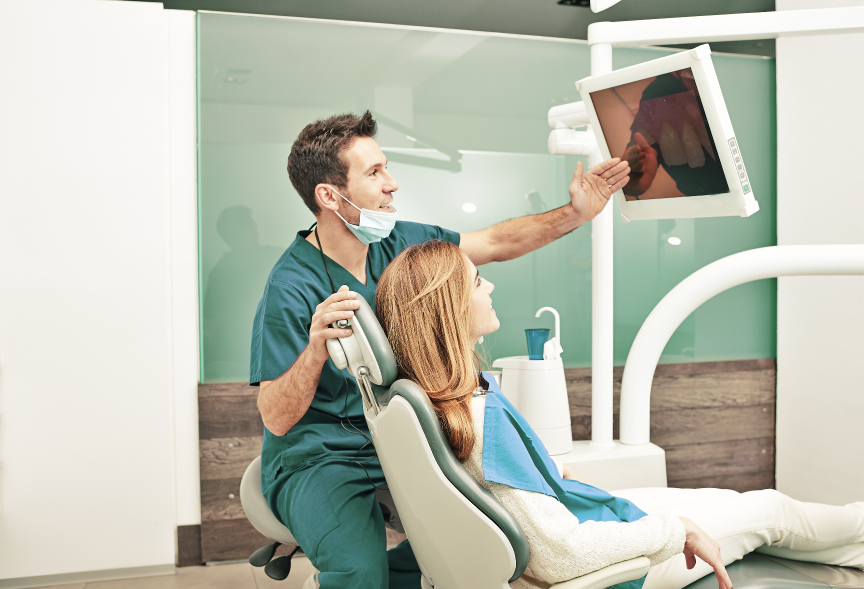 Dentist showing X-ray image to female patient on screen during consultation in dental clinic
