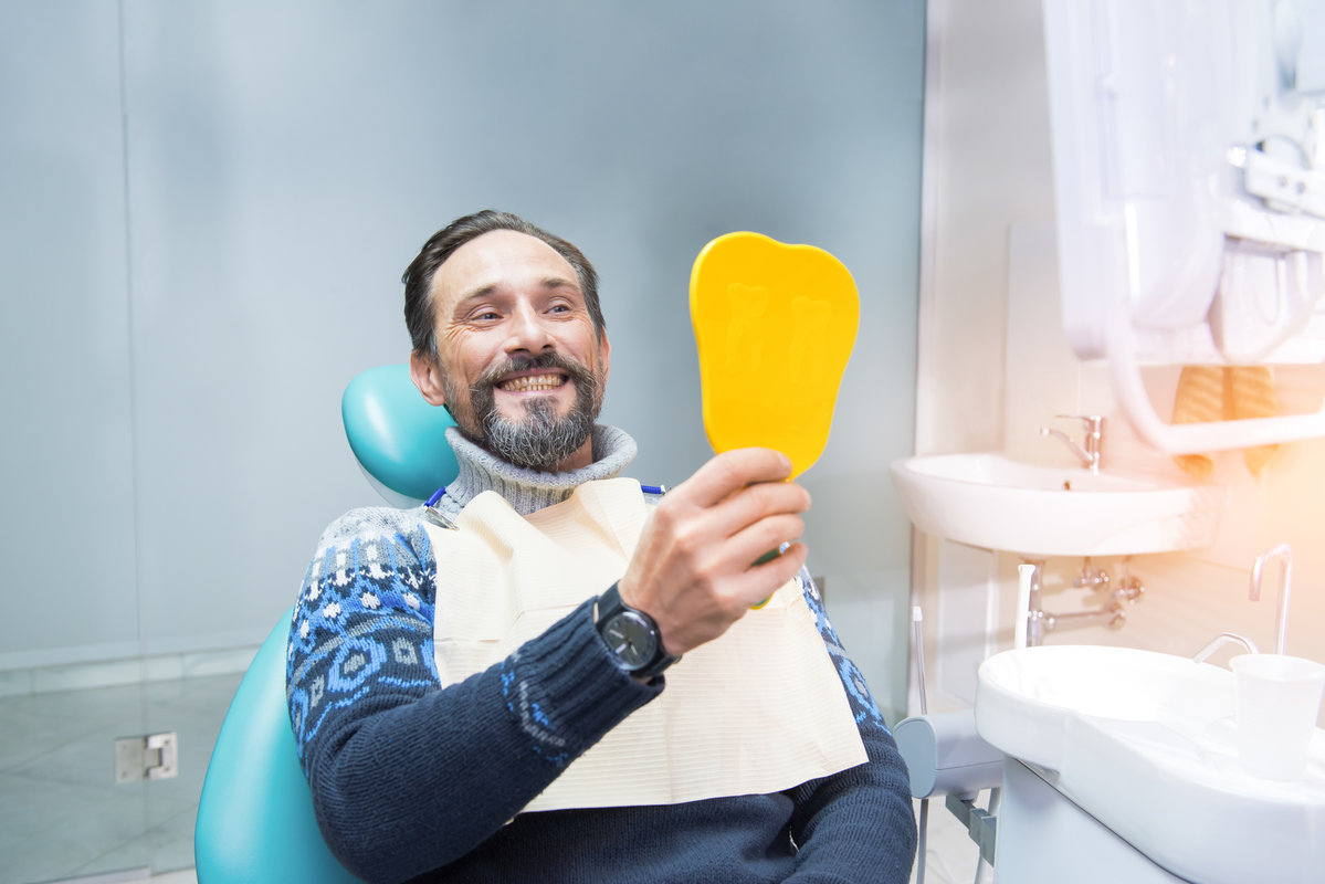 Man in dental chair. Person holding mirror and smiling. Fix your smile.