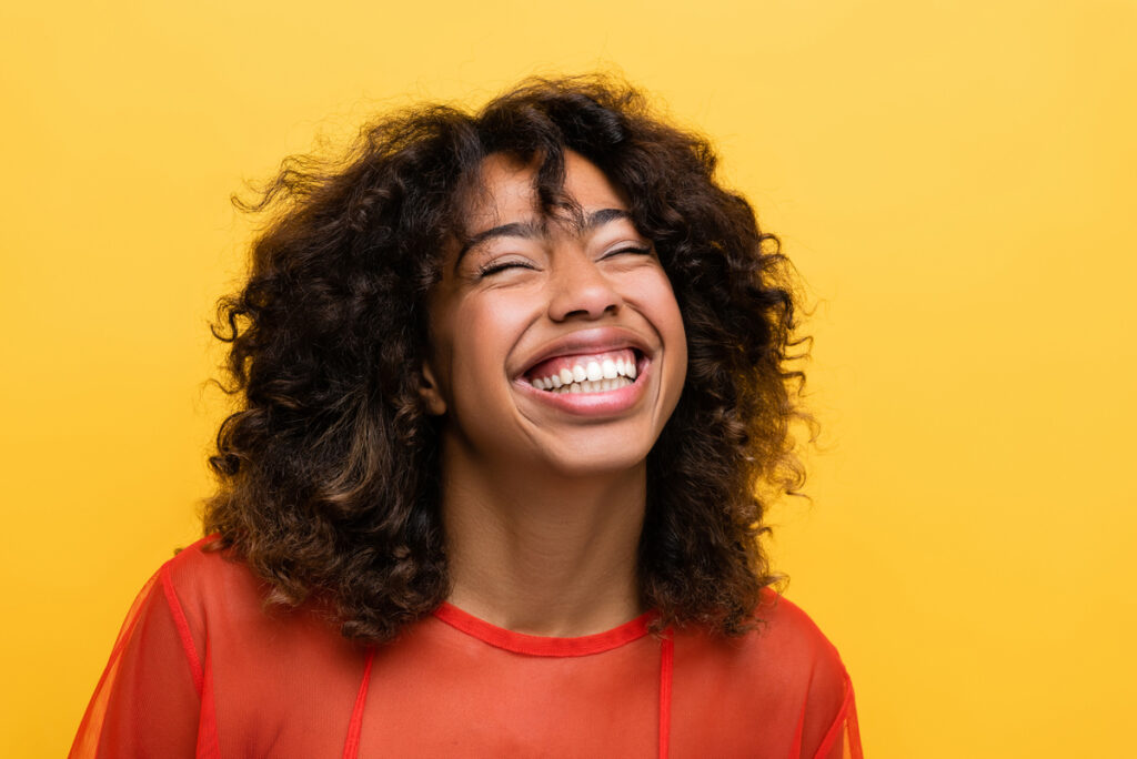 overjoyed african american woman smiling with closed eyes isolated on yellow.