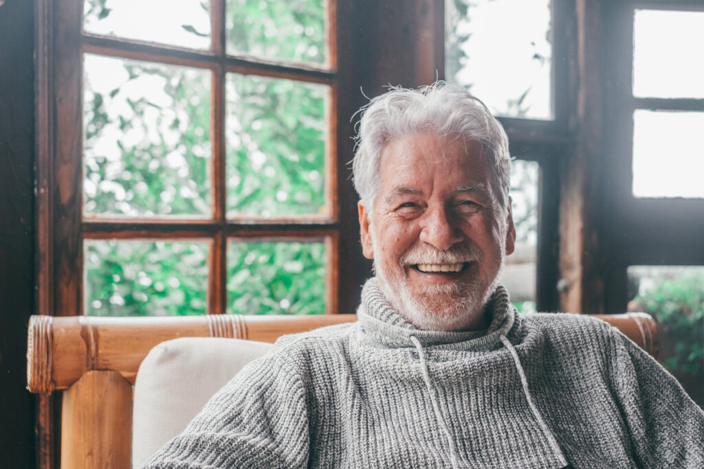 Portrait of old man smiling and looking at the camera sitting on the sofa from home. Closeup male person senior cheerful indoor.