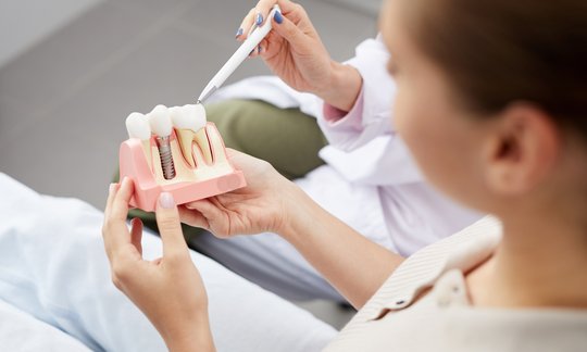 Dentist showing a patient a tooth model during a dental crown consultation